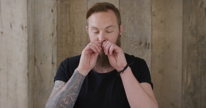 young hipster punk man touching beard looking pensive attractive caucasian male on wooden background