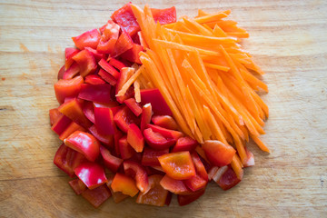 Kitchen still life. Fresh raw red sweet pepper with carrot are sliced on the wooden cutting board.