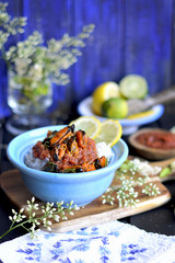 rice with seafood, in tomato sauce. with lemon and lime. On a blue wooden background, decorated with a bouquet of spring flowers of white. Serving with a napkin with vintage embroidery