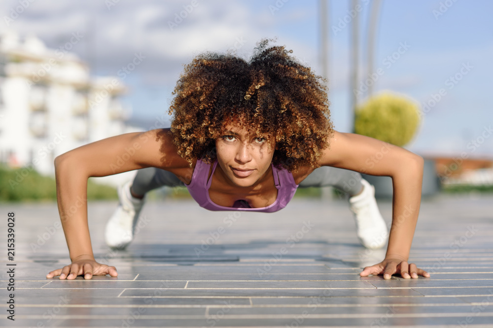 Wall mural Black fit woman doing pushups on urban floor.