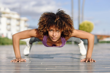 Black fit woman doing pushups on urban floor.
