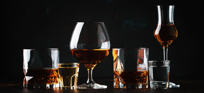 Set of strong alcoholic drinks in glasses and shot glass in assortent: vodka, rum, cognac, tequila, brandy and whiskey. Dark vintage background, selective focus