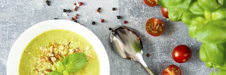 green cream soup on the white bolw, spoon, cherry tomatoes, black and red grainy pepper, grey background