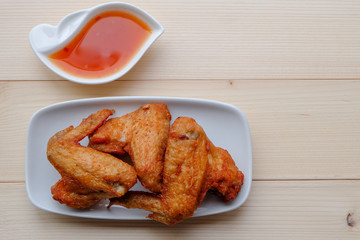Top view and close up: Deep Fried Chicken wing in white plate with sweet sauce on wooden background. Popular food for kids.