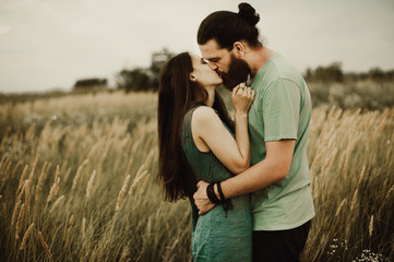 Hipster Couple on field kissing. Bearded man with a girl with long hair outdoors.