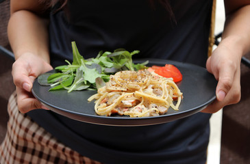 The Spaghetti Carbonara with green vegetable and red tomatoes cut into pieces in hands to serve.