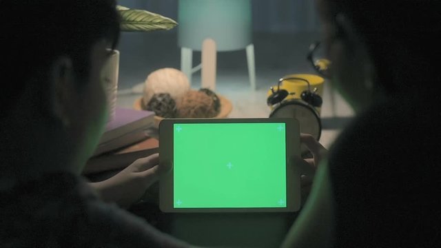 Over the shoulder shot of a woman and boy looking at tablet with a key-green screen.
