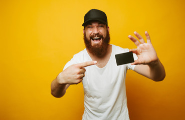 Portrait of a cheerful bearded man pointing finger at credit card isolated over yellow background