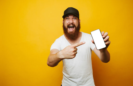 Amazed young bearded man in white t-shirt pointing at phone
