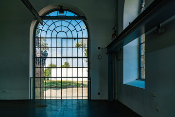 Innenraum eines alten Fabriksgebäudes mit großem Rundbogenfenster mit Ausblick auf das verlassene Fabriksgelände