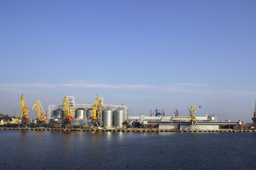 Fototapeta na wymiar Cranes and granaries, cisterns with wheat in the port in clear weather, the sea.