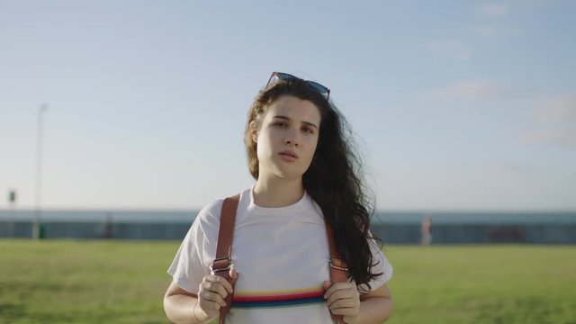 portrait of beautiful young independent woman tourist looking serious at camera in beautiful sunny seaside park