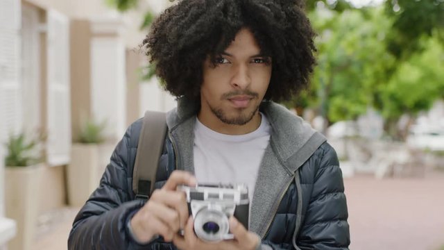portrait of young mixed race photography student man taking photo using retro camera smiling enjoying sightseeing in urban city background