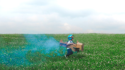 Cute little dreamer kid boy wearing blue helmet and aviator glasses flying in a cardboard airplane...