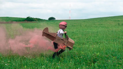 Cute little dreamer kid girl wearing pink helmet and aviator glasses flying in a cardboard airplane with attached smoke bombs through the field, pretending to be a pilot © supamotion