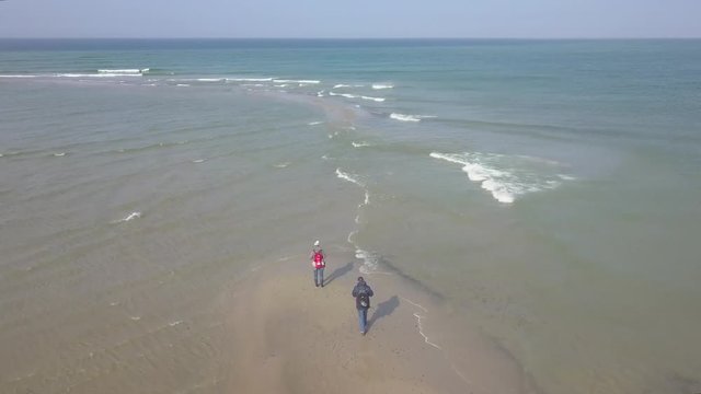 Drone flying over two people standing at the northernmost shore of Grenen, Denmark. This is where the Baltic Sea and the North Sea meet.