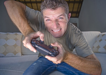 Naklejka premium lifestyle portrait of young stressed and excited gamer man playing video game at home living room having fun on sofa couch holding controller concentrated
