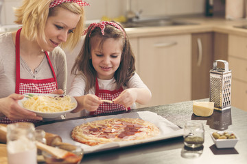 Little girl putting cheese on the pizza dough