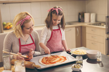 Little girl spreading ketchup over the pizza dough