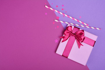 .Purple classic gift box with shiny satin bow and paper striped cocktail straws with confetti in...