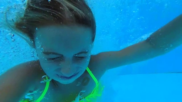 Little girl jumping in the swimming pool. Cute teen girl swimming underwater in the pool