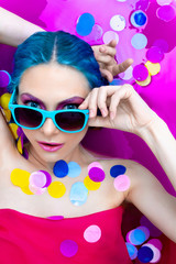 Portrait of young sexy female girl adult woman / fashion luxury model with blue hair relaxing wearing turquoise sunglsses in bath isolated by pink water with colorful confetti. Skin care, beauty