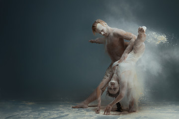 Fototapeta na wymiar Dancing in flour concept. Girl woman female and muscle fitness guy man male couple in love and in relationship making dance element prefomance in flour / white dust on isolated black / grey background