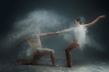 Dancing in flour concept. Girl woman female and muscle fitness guy man male couple in love and in relationship making dance element prefomance in flour / white dust on isolated black / grey background