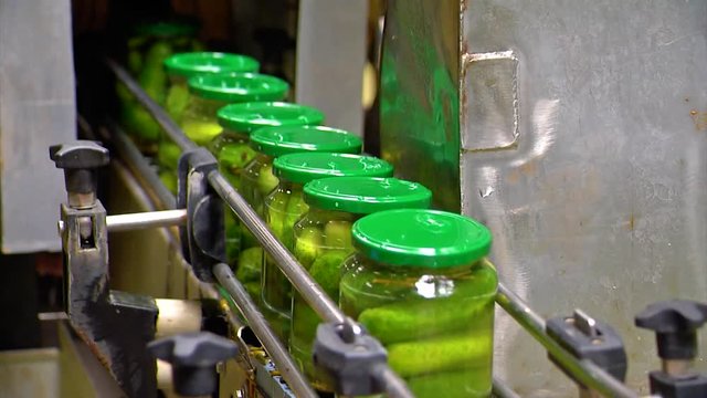 Canned cucumbers. Glass jars with cucumbers and spices on the conveyor