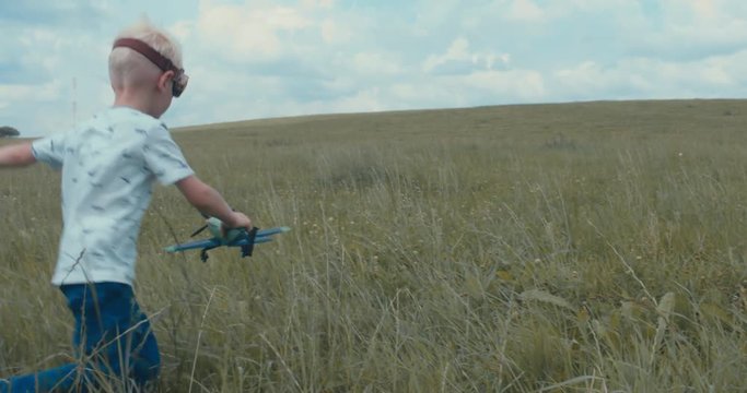 Cute little dreamer kid boy wearing pilot glasses playing with toy airplane in the field, DX. 4K UHD 60 FPS SLO MO 