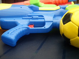 Close up soccer ball with yellow and black and three water guns in electric bright colors yellow, blue, green and red