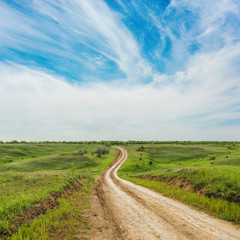 Fototapeta na wymiar rural road in green meadow and clouds over it