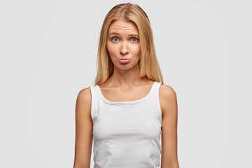 Obraz premium Cute young female purses lower lips and looks with displeased expression, wears casual t shirt, feels offended after quarrel with boyfriend, isolated over white background. People and lifestyle