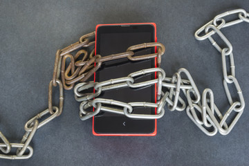 Technology addiction concept, smartphone and chains on the dark background.