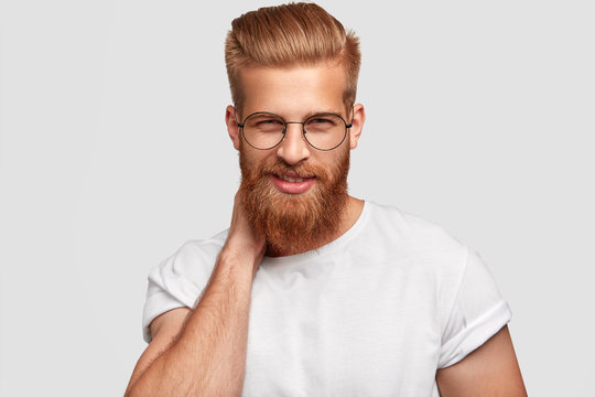 Cheerful ginger male with thick beard and mustache, looks mysteriously through spectacles, wears casual shirt, ready for work stands alone against white background. People, emotions, lifestyle concept