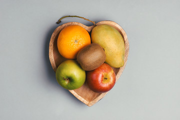 Orange, mango, apple and kiwi in a wooden heart-shaped plate