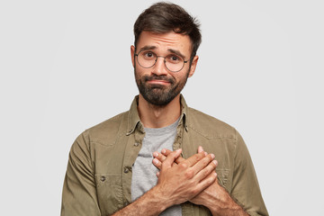 Oh, thank you very much! Attractive unshaven young male keeps hands on heart, expresses gratitude, stands against white studio wall. Friendly bearded Caucasian guy being thankful to best friend - Powered by Adobe