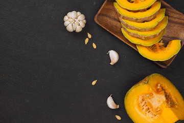 Orange pumpkin sliced in white dish on black stone background.