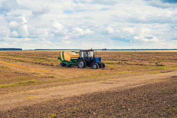 Obraz premium Grain harvesting equipment works in the field. Countryside landscape and cloudy sky. Rural field and sky horizon