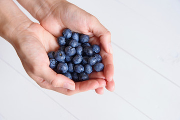 Obraz na płótnie Canvas Fresh blueberries in women's hands on a white wooden background. Top view.