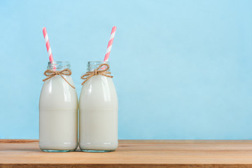 a bottle of milk with straw on wooden table, blue background