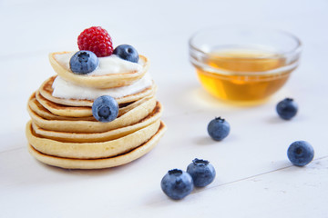 Homemade delicious pancakes with yogurt, fresh blueberries, raspberries and honey on white wooden background. Concept of tasty and healthy food.