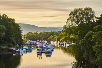Scenic sunset view of Balloch harbour near Loch Lomond with floating boats reflected in river...