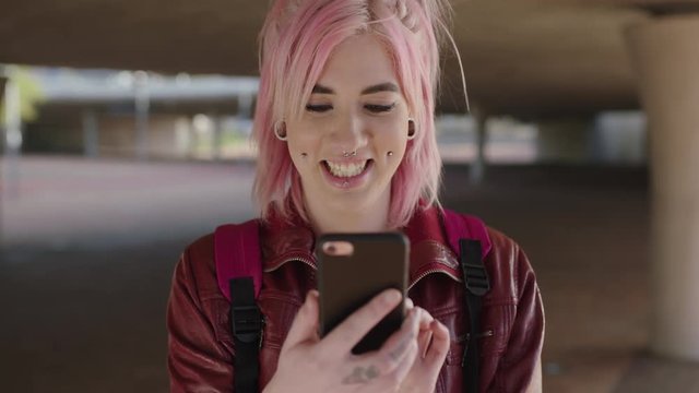 portrait of alternative punk woman with pink hair texting browsing social media using smartphone urban background
