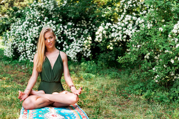 Beautiful young blonde meditating in lotus position in park