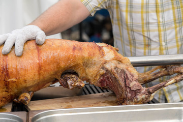 Cutting the mutton hulk fried on a grill for the Uzbek pilaf. Male hands keep a povarsky knife in gloves and cut meat