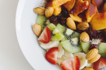 Sweet and healthy breakfast meal: oats with strawberry, kiwi, banana, peach, dried cranberry and almond