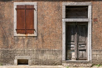 Rostiger Fensterladen und alte Holztür an sonniger Fassade