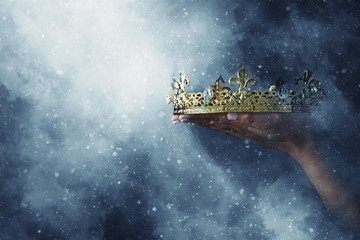 mysteriousand magical image of woman's hand holding a gold crown over gothic black background....