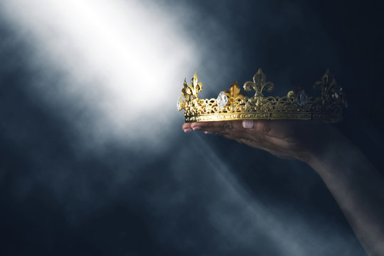mysteriousand magical image of woman's hand holding a gold crown over gothic black background. Medieval period concept.